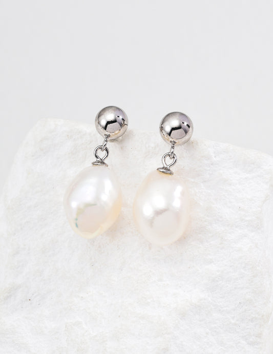Silver ball and teardrop pearl drop earrings on a textured display