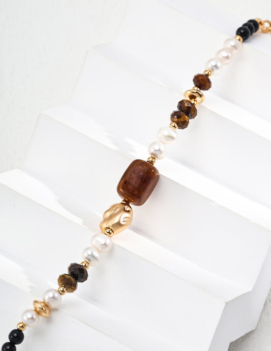 Beaded bracelet close-up with brown stone, gold spacers, white pearls, and black beads