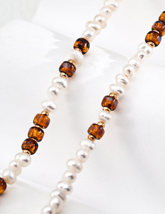 Strand necklace detail with white pearls and amber cube beads on gold-tone links