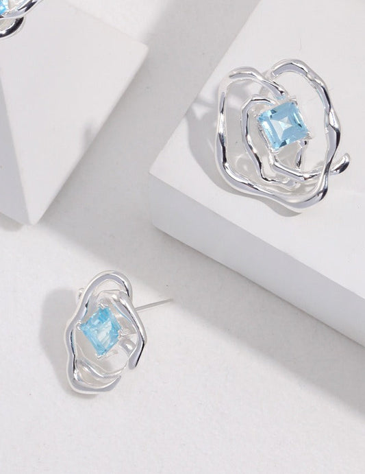 Silver-tone asymmetrical stud earrings with blue square gemstone in raised openwork setting
