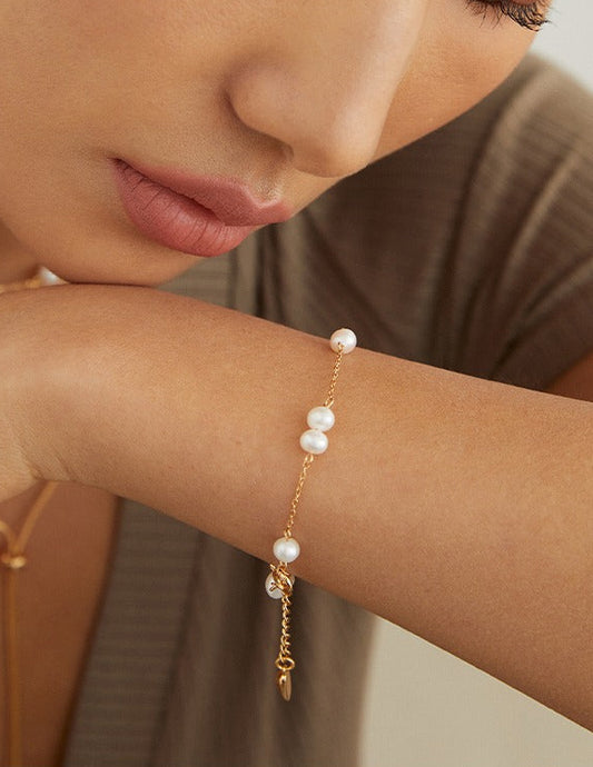 Gold pearl bracelet on wrist with three round white beads and a dangling charm