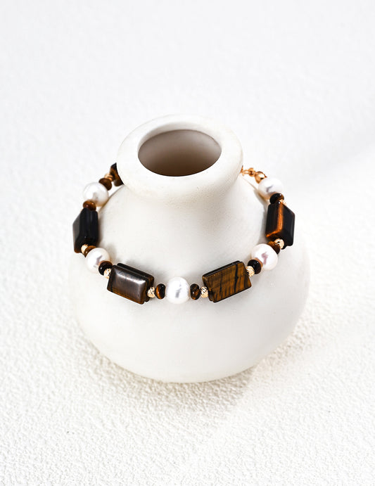 Gold-tone beaded bracelet with tiger eye and white pearl beads on a white stand