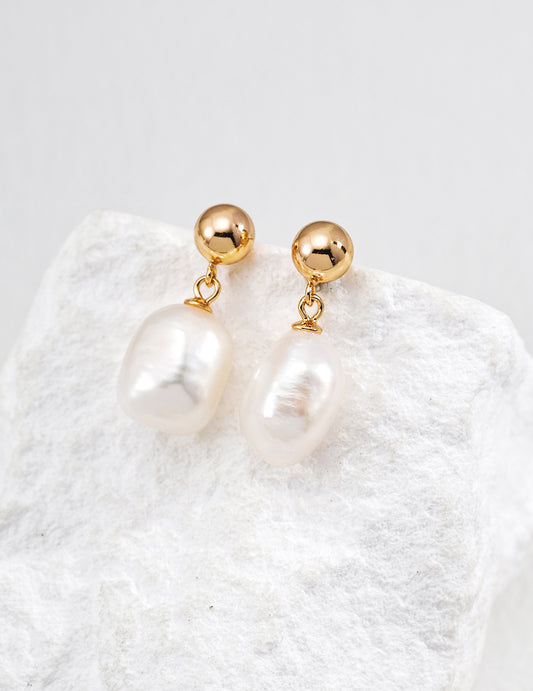 Gold ball and teardrop pearl drop earrings on a textured display