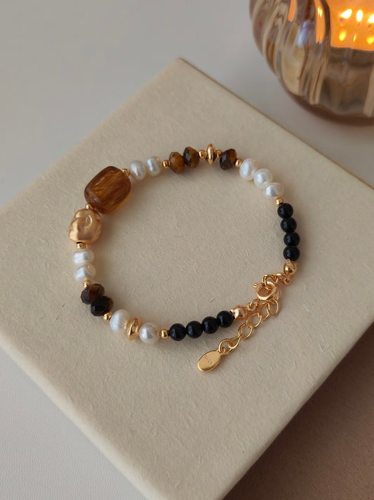 Beaded bracelet on jewelry box: white pearls, black beads, brown stones, and gold charm