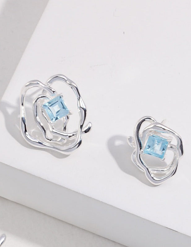 Silver-tone asymmetrical earrings with blue square gemstone, close-up view