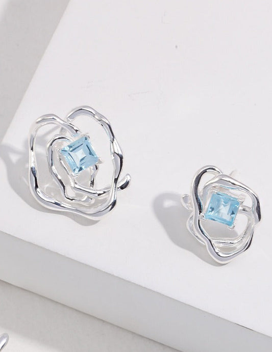 Silver-tone asymmetrical earrings with blue square gemstone, close-up view