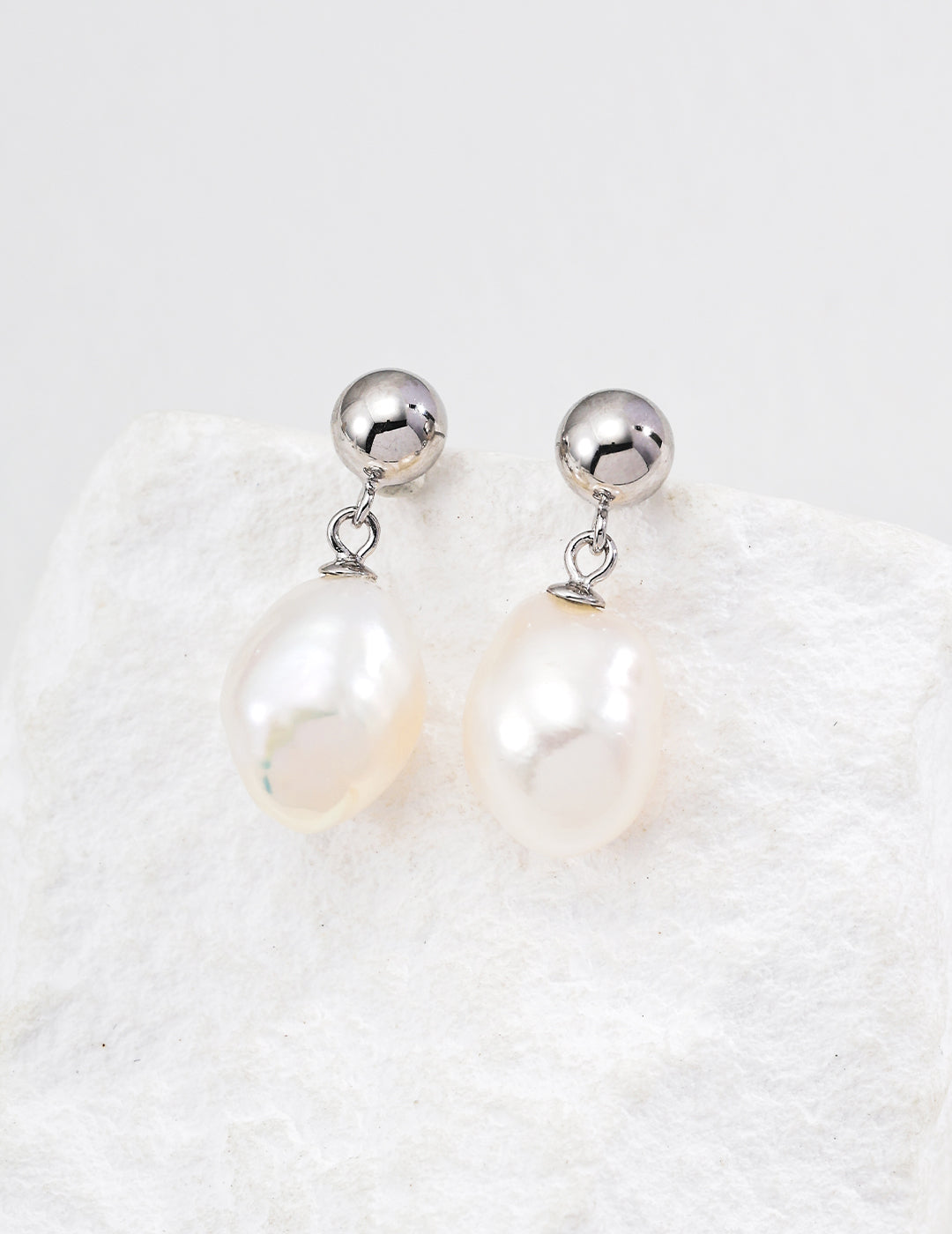Silver ball and teardrop pearl drop earrings on a textured display