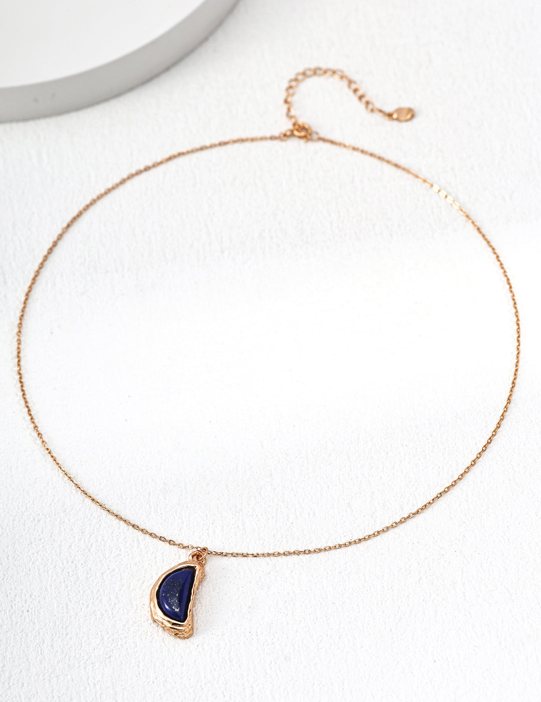 Gold-tone teardrop lapis pendant necklace lying on white display