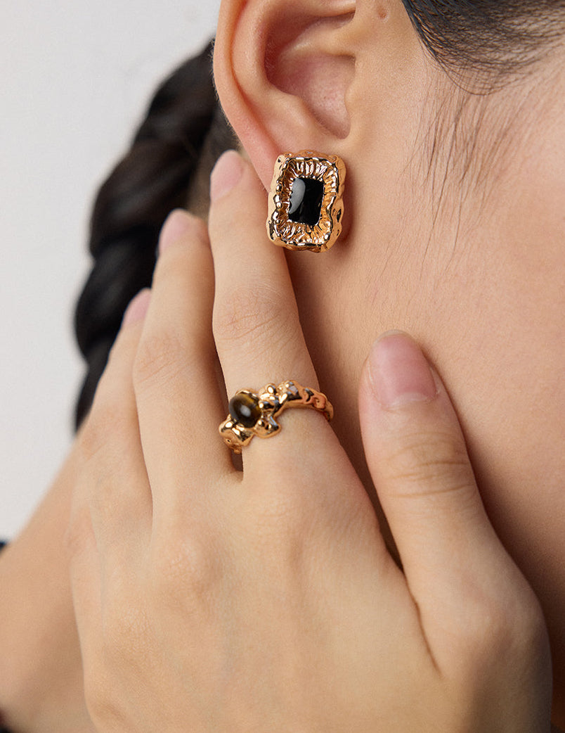 Gold-tone ring on finger with dark square cabochon centerpiece in ornate bezel