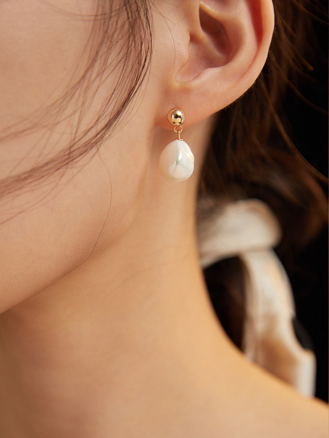 Gold ball and teardrop pearl drop earrings on a model’s ear
