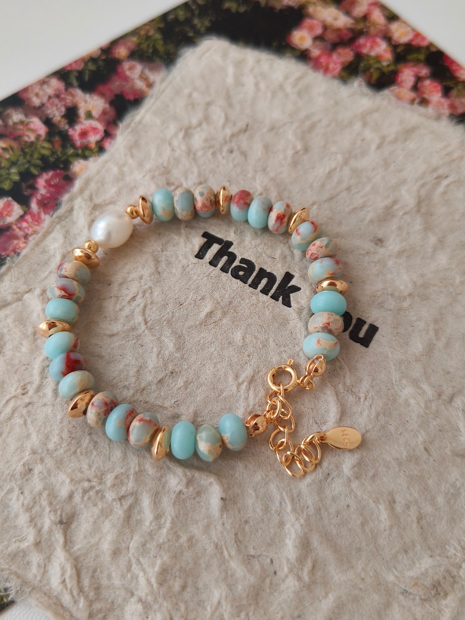 Gold-tone beaded bracelet with turquoise beads, central white pearl, and dangling charm details