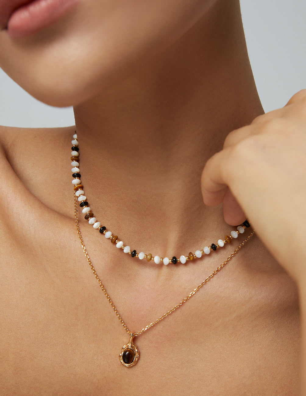 Layered gold-tone necklaces: multicolor bead choker and oval dark stone pendant
