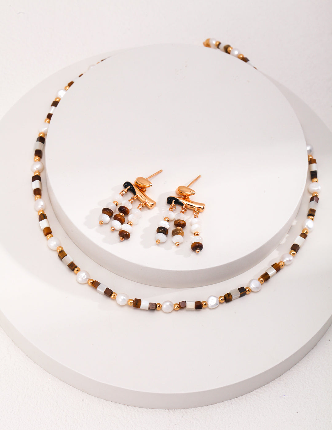 Gold-tone stud earrings with pearl and tiger eye bead drops on display