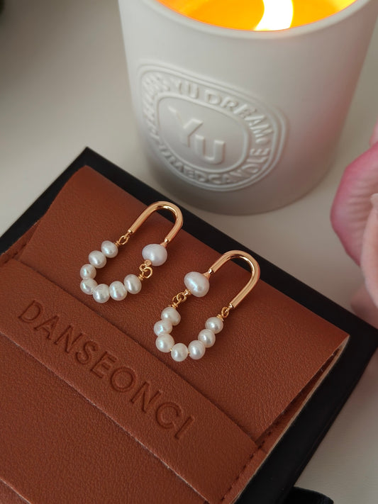Dangling rose gold hoop earrings featuring white pearl clusters on the front-facing pair