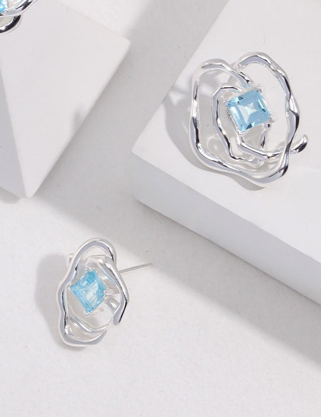 Silver-tone asymmetrical stud earrings with blue square gemstone in raised openwork setting