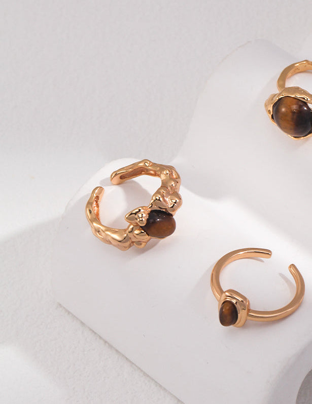 Gold-tone rings with tiger eye cabochons on display, including an open band style