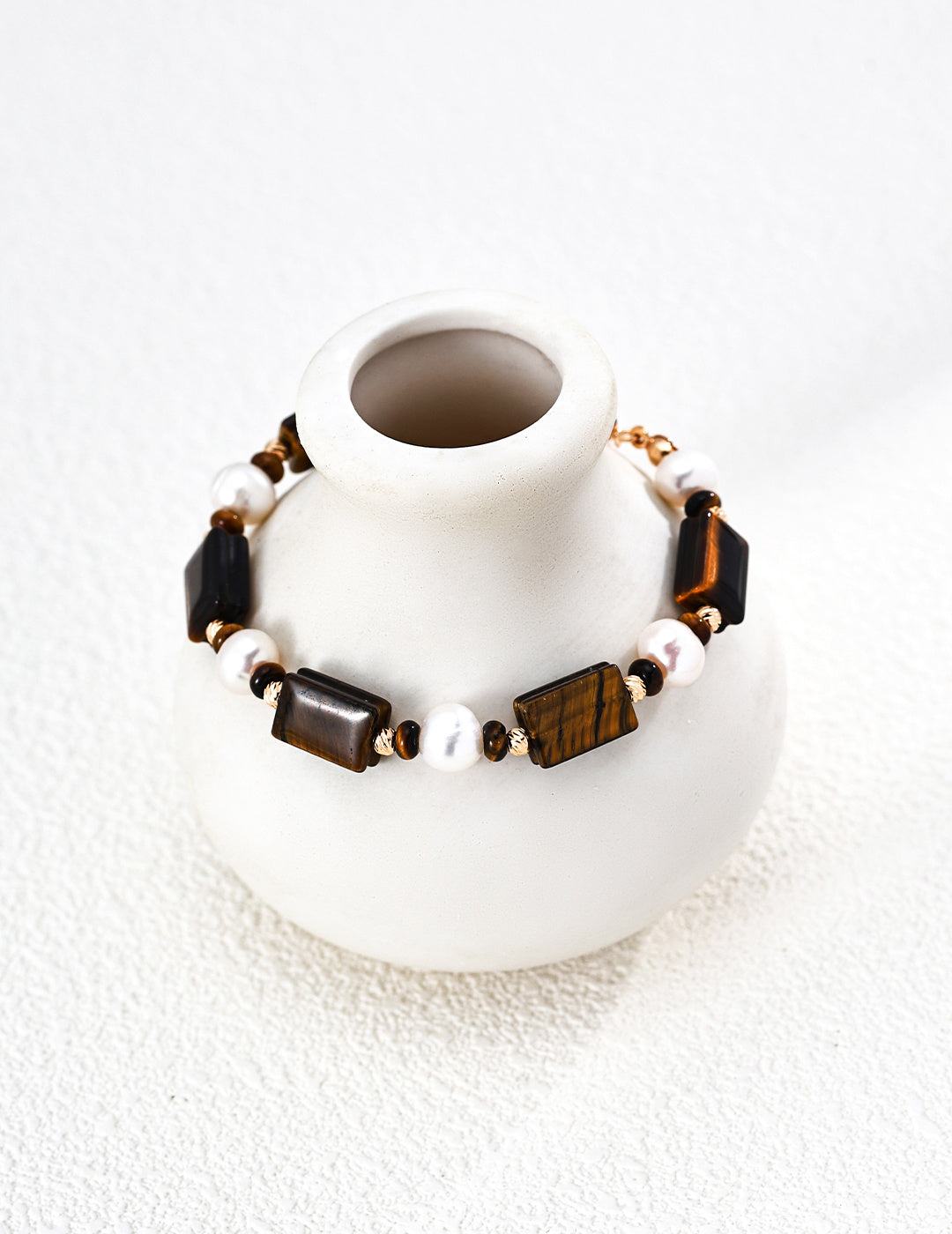 Gold-tone beaded bracelet with tiger eye and white pearl beads on a white stand