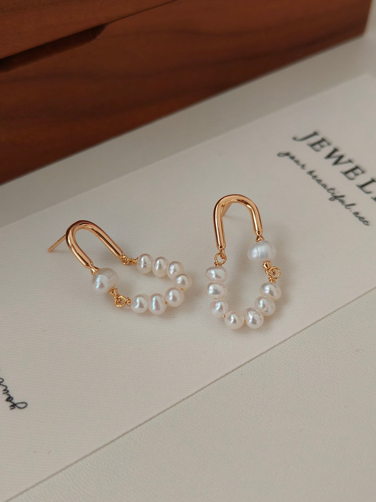 Rose gold hoop earrings with multiple white pearls in a rounded dangling cluster