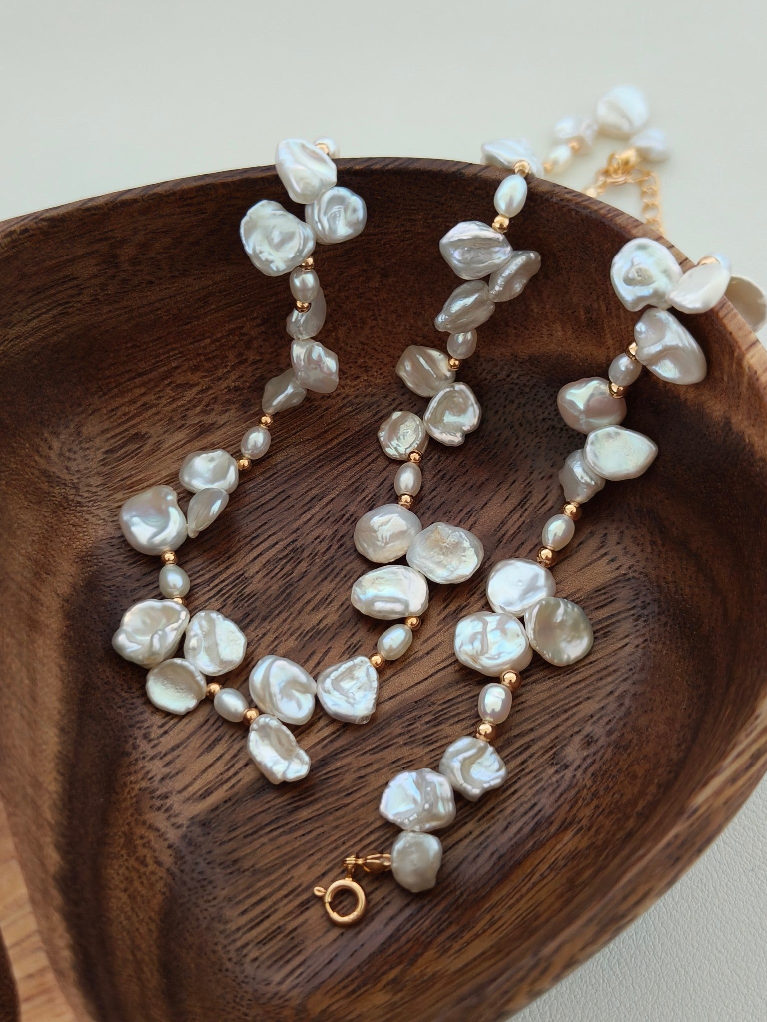 Freshwater pearl necklace draped on wooden tray; baroque pearls and gold clasp
