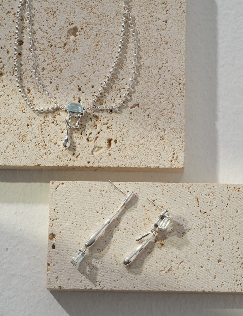 Silver necklace with blue square gemstone centerpiece and dangling hook charm