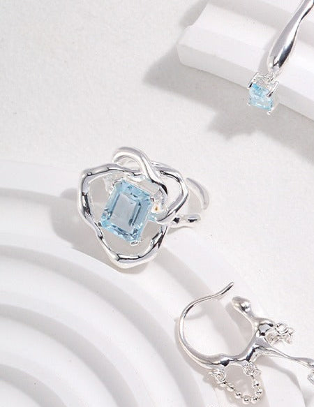 Silver ring with rectangular light-blue gemstone on a white pedestal, angled view
