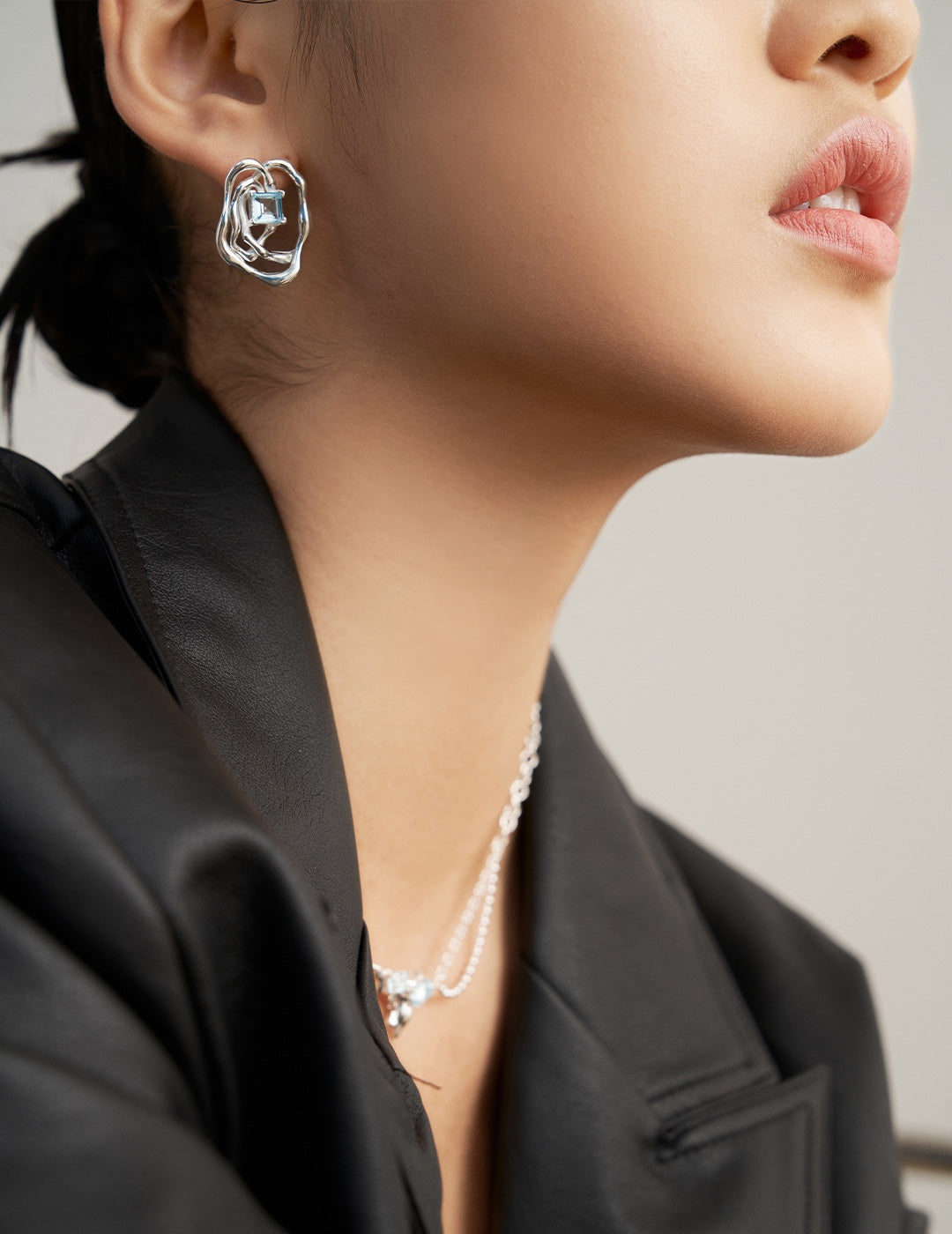 Asymmetrical silver-tone earrings with blue square gemstone, worn on model's ear