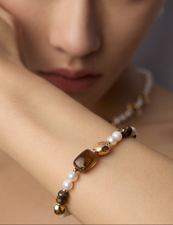 Close-up bracelet on arm with white pearls, black beads, brown tiger eye beads, and gold accents