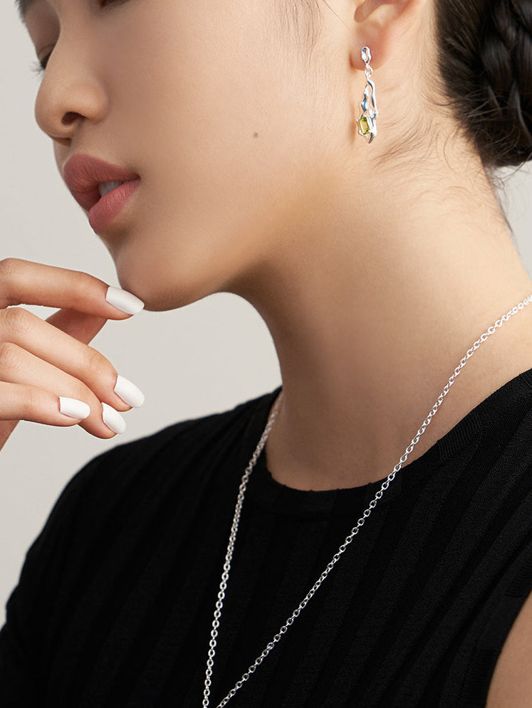 Silver peridot green gemstone drop earrings on ear with wavy abstract design