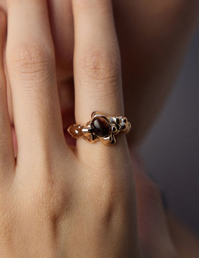 Gold-tone statement ring on hand with dark oval tiger eye cabochon in raised setting