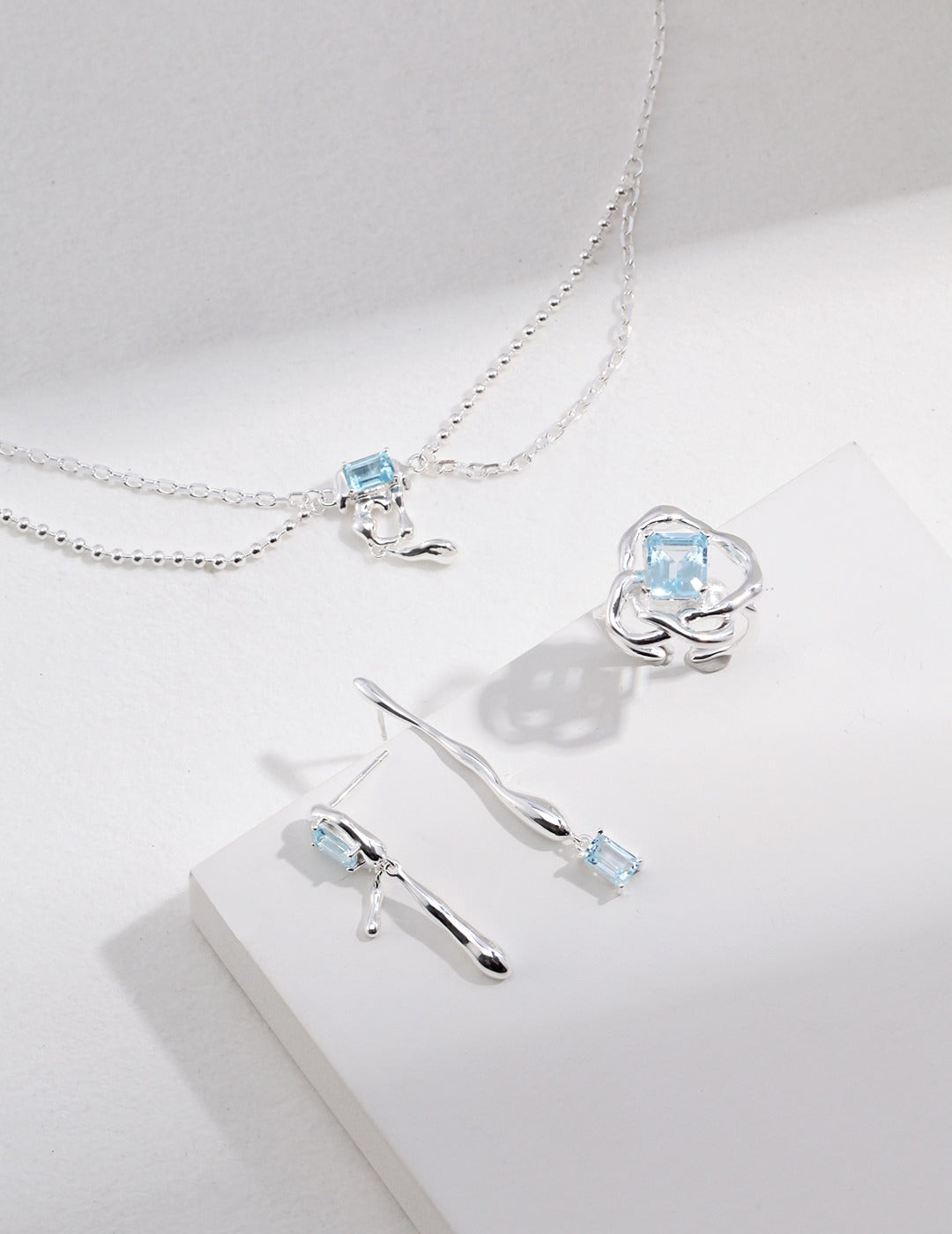 Silver necklace with light blue square centerpiece and hook-shaped pendant
