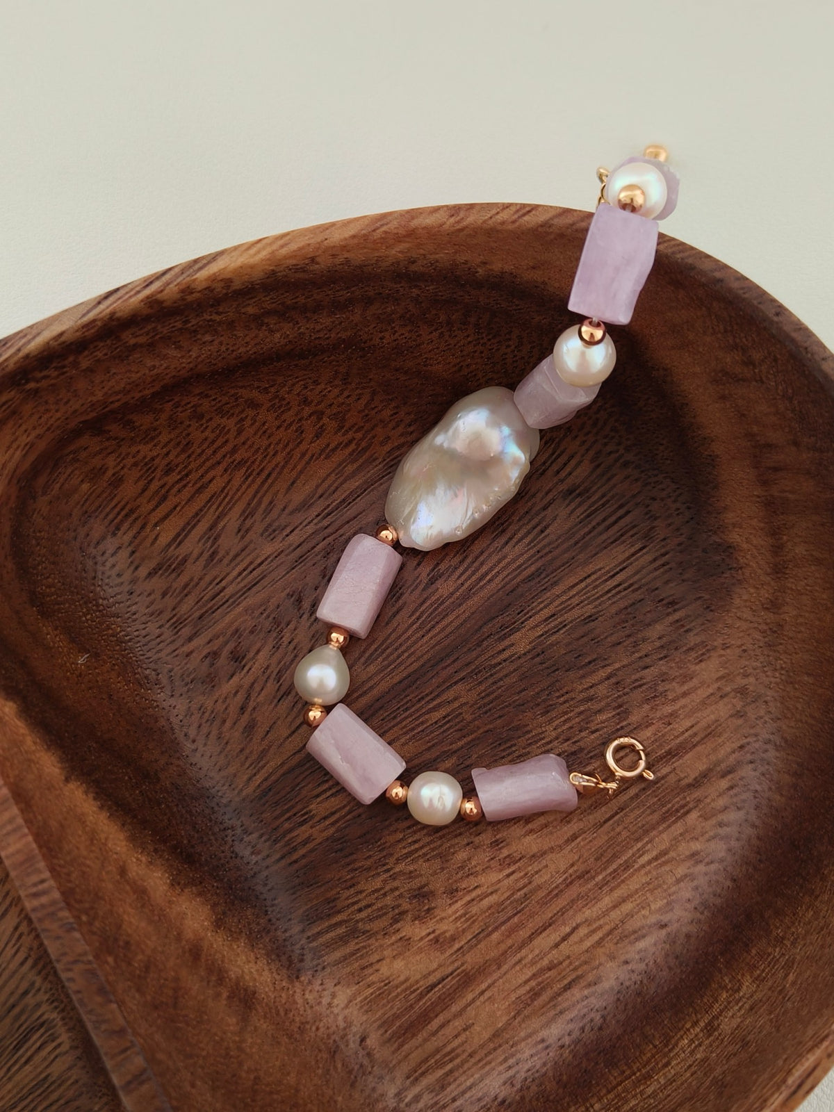 Purple stone and pearl charm bracelet with gold chain detail on wooden dish