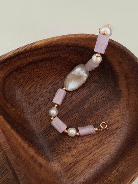 Purple stone and pearl charm bracelet with gold chain detail on wooden dish
