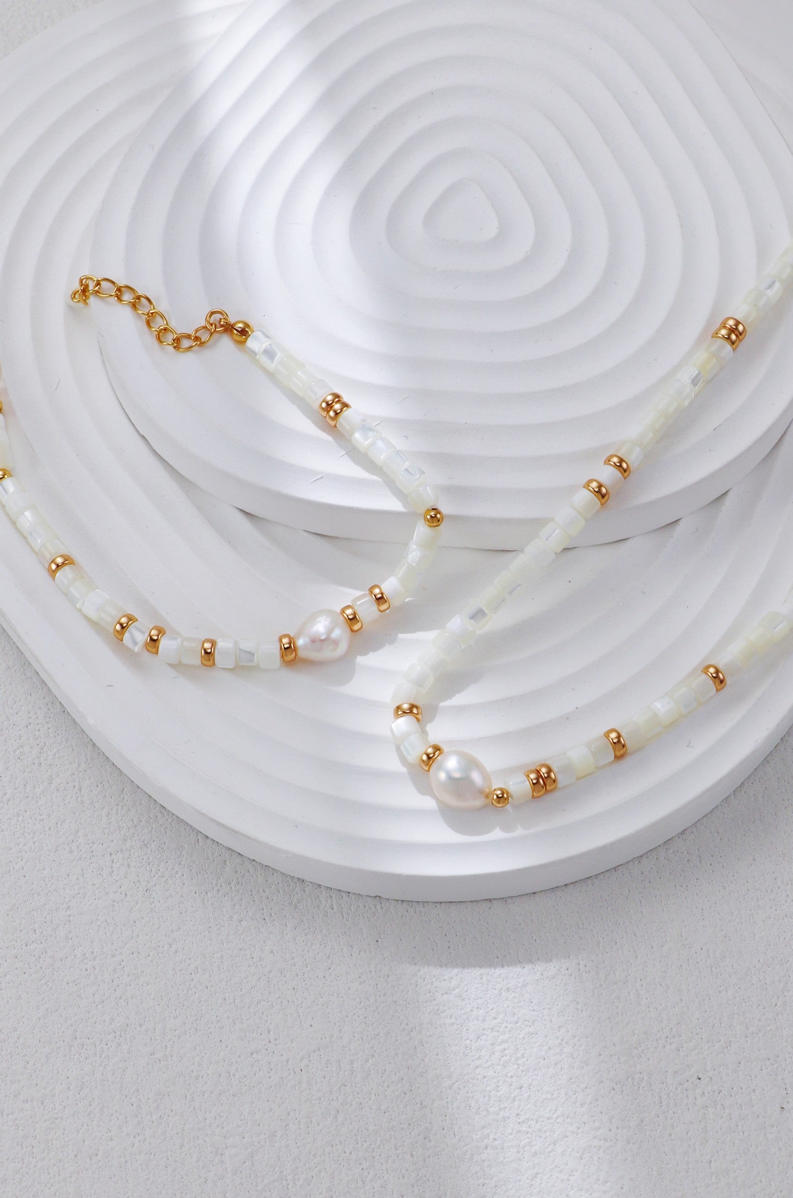 White shell bead necklace with gold micro-beads and two pearls at center.
