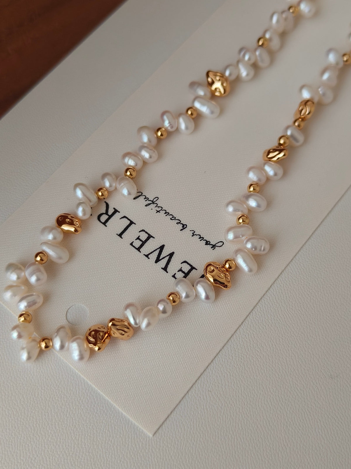Freshwater pearl necklace detail with gold-tone accents and heart clasp on card
