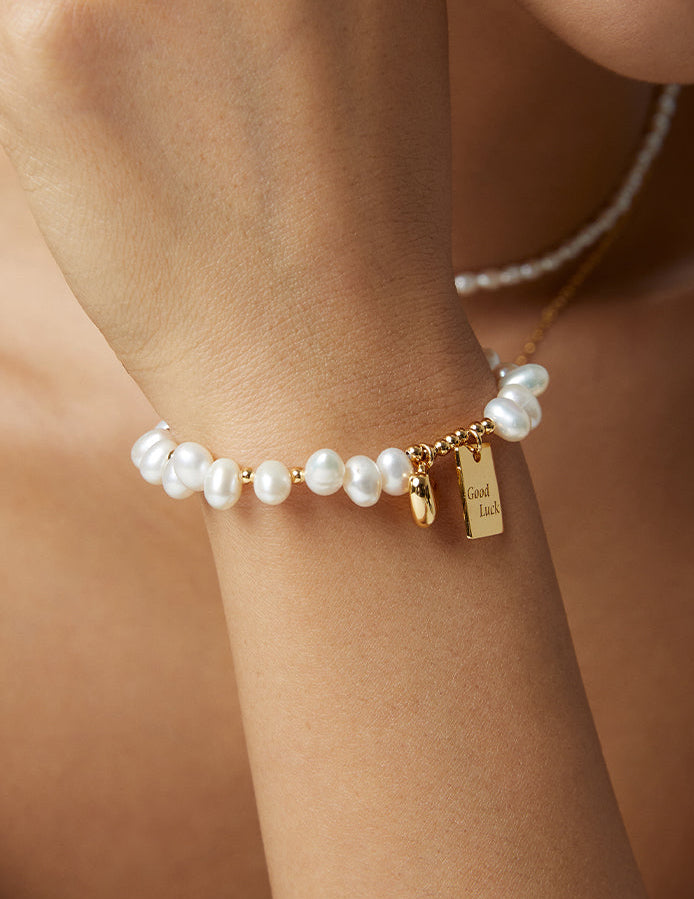 Pearl beaded bracelet on wrist with gold Good Luck charm