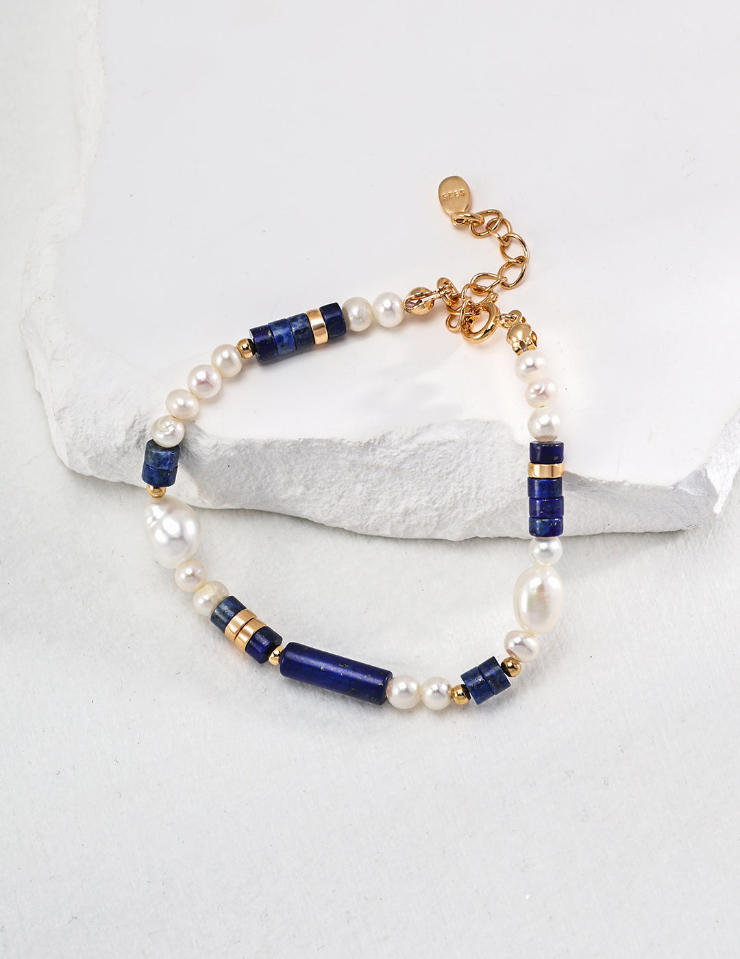 Freshwater pearl and lapis bead bracelet with gold clasp on stone surface