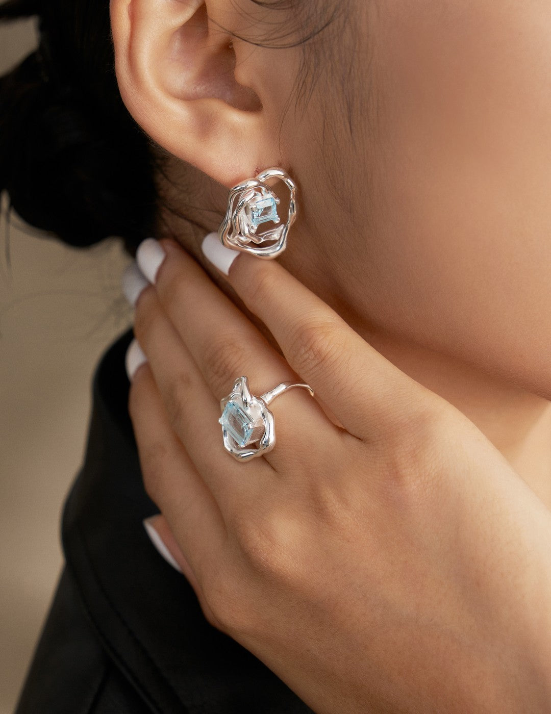 Silver-tone asymmetrical earrings with blue square gemstone, worn on model's ear