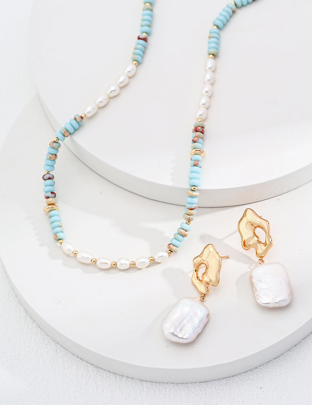 Turquoise and freshwater pearl bead necklace with gold-tone accents, draped on stand