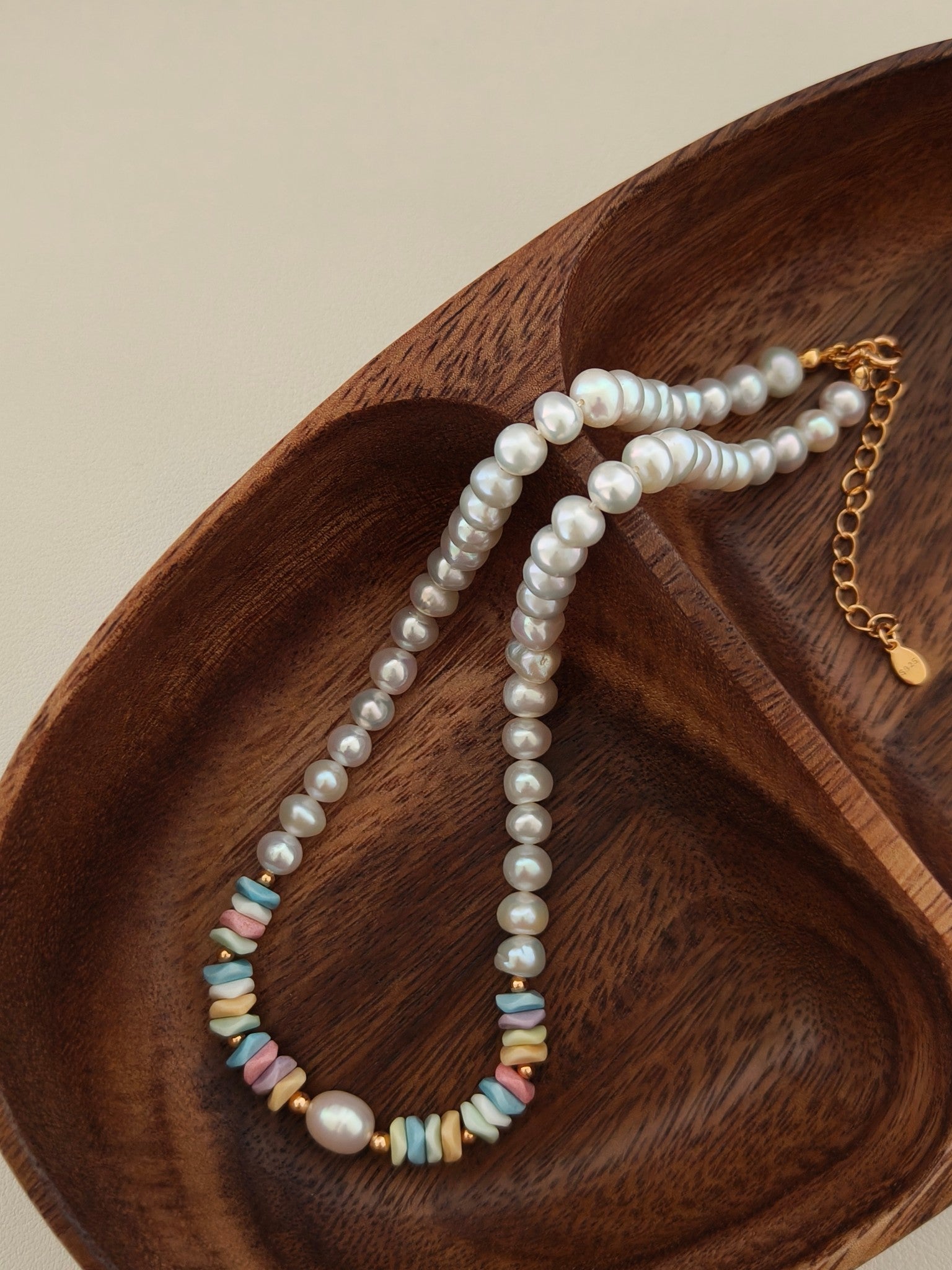 Pearl necklace laid across wood with rainbow stone bead accents and gold chain.