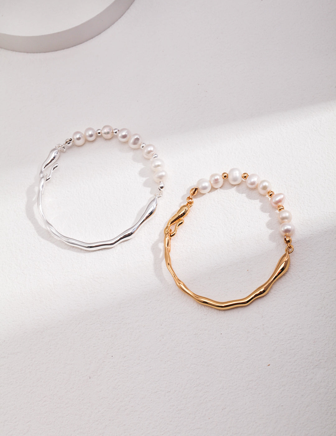 Pair of pearl bracelets with wavy chain links, one gold-tone and one silver-tone