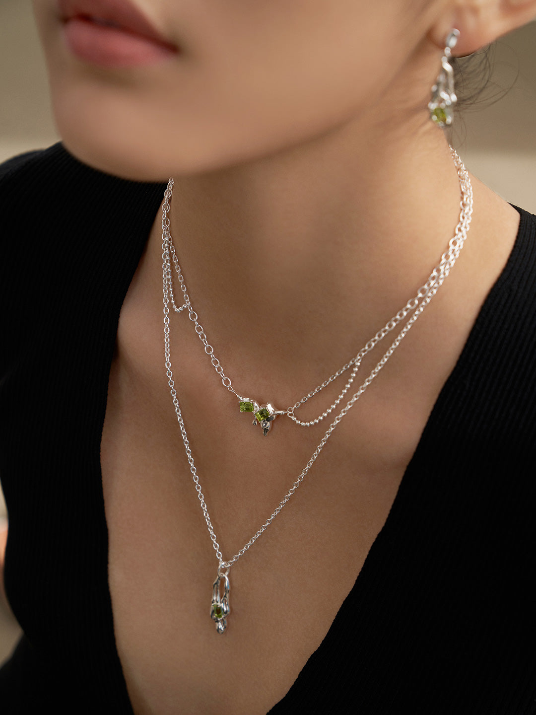 Close-up layered silver necklace with green peridot charms and teardrop pendant