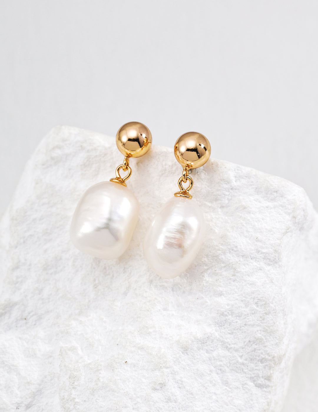 Gold ball and teardrop pearl drop earrings on a textured display