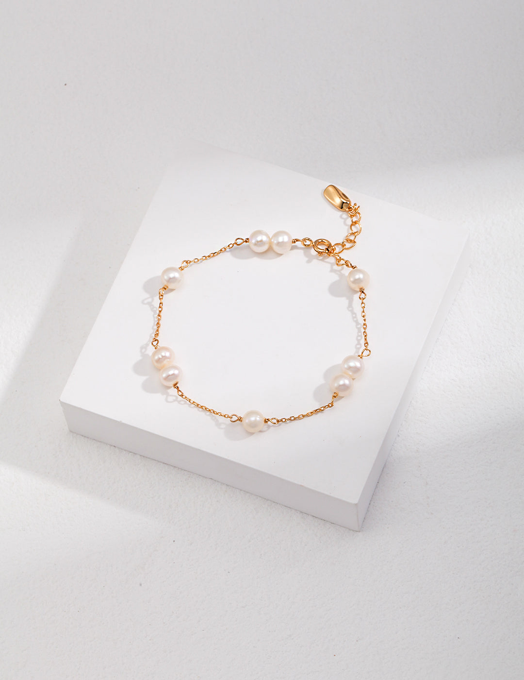 Gold-toned pearl bracelet with round white beads and a small teardrop charm