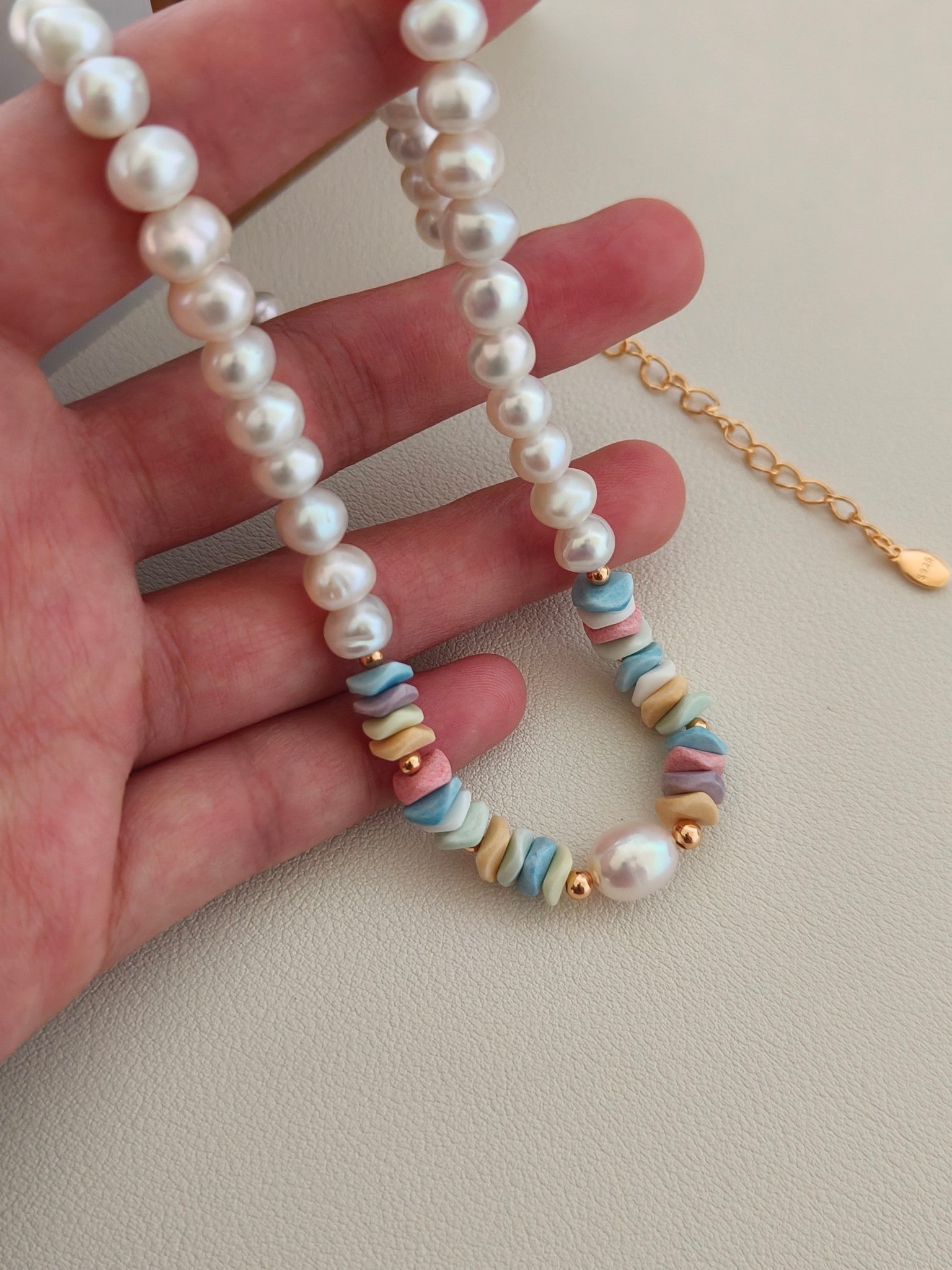 Pearl and rainbow stone bead necklace held in hand, with gold-toned chain detail.