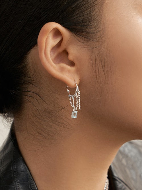 Blue topaz drop earrings in silver tone with chain fringe, worn on ear
