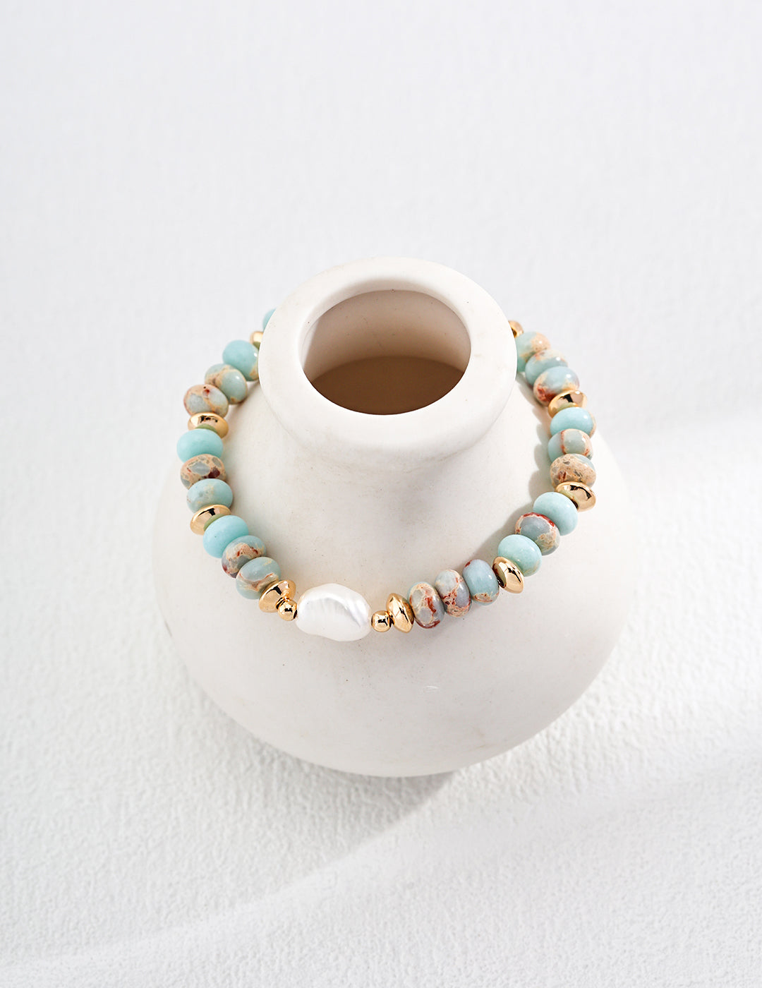 Gold-tone beaded bracelet with turquoise stones and a white pearl bead on a fabric display