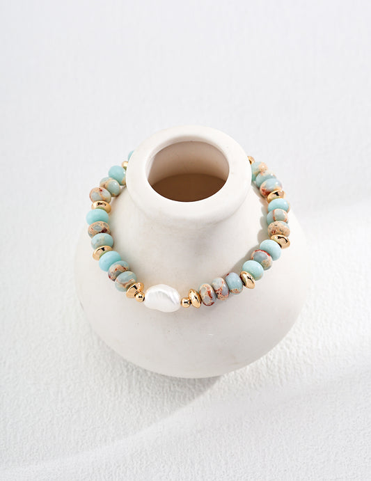 Gold-tone beaded bracelet with turquoise stones and a white pearl bead on a fabric display