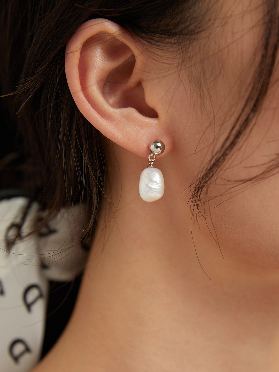 Silver ball and teardrop pearl drop earrings on a model’s ear