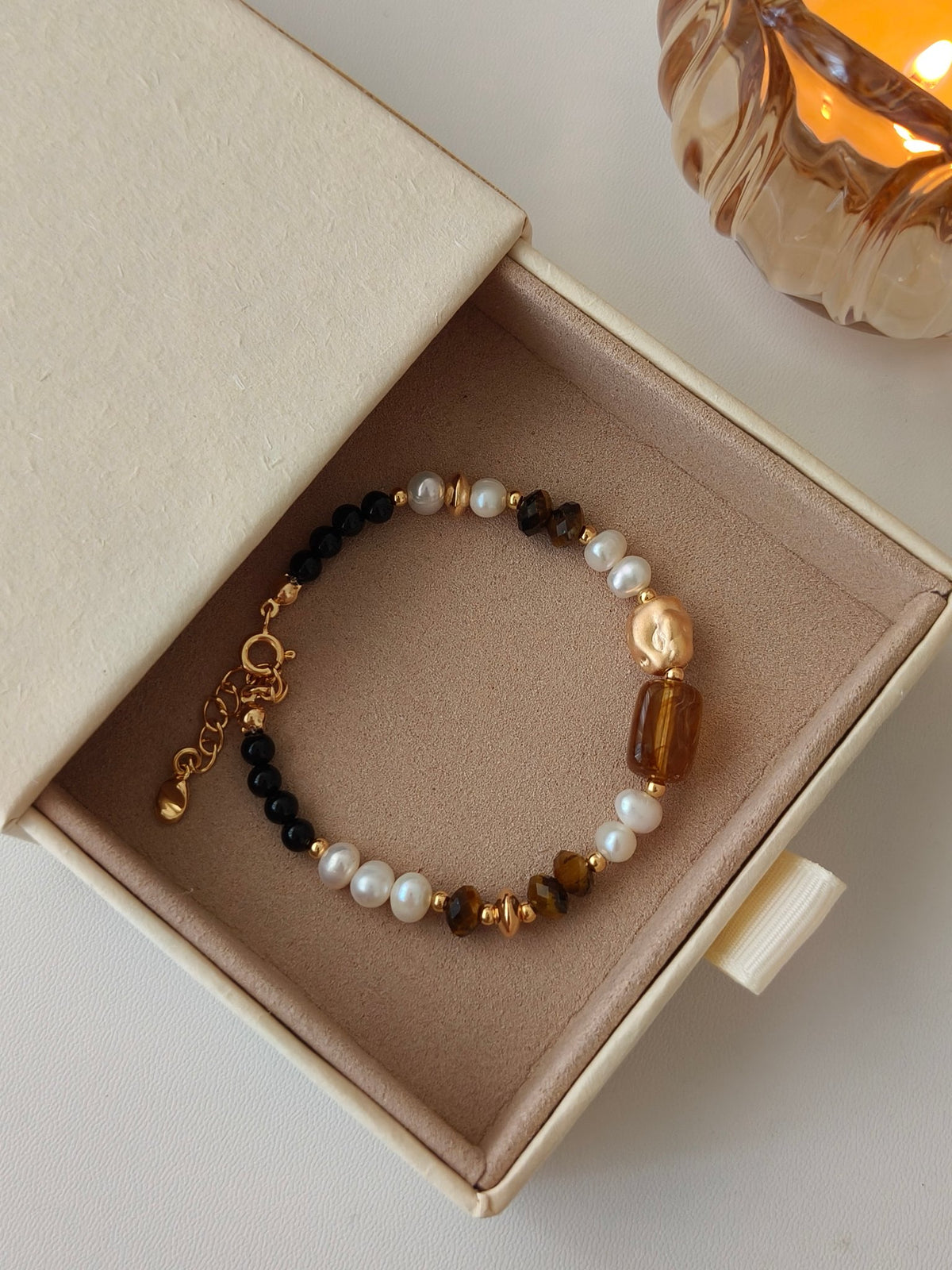 Beaded bracelet in jewelry box with white pearls, dark beads, and brown tiger-eye stones