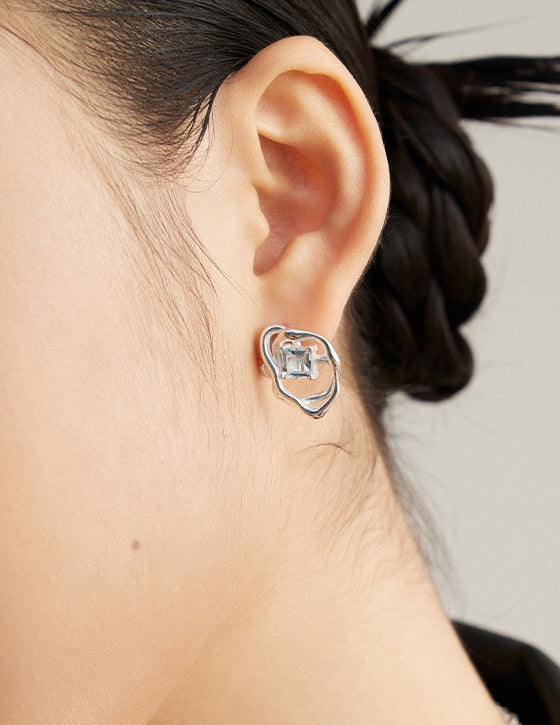 Silver-tone asymmetrical earrings with blue square gemstone, close-up on ear